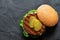 Freshly grilled plant based burger patty in bun with lettuce, slices of gherkin  and sauce isolated on black slate. Top view. Copy