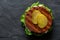 Freshly grilled plant based burger patty on bun with lettuce, slices of gherkin and sauce isolated on black slate. Top view. Copy
