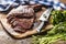 Freshly grilled tomahawk steak on slate plate with salt pepper rosemary and parsley herbs. Sliced pieces of juicy beef steak