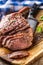 Freshly grilled tomahawk steak on slate plate with salt pepper rosemary and parsley herbs. Sliced pieces of juicy beef steak