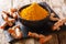 Freshly ground turmeric in a black bowl and fresh root close-up. horizontal