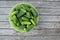 Freshly harvested small cucumbers are in a large green bowl. A plastic bowl stands on a wooden table. Harvest, harvesting