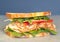 Freshly made deli style sandwich with lettuce, several different kinds of vegetables, tomatoes, cheese, meats similar to ham,