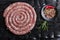 Freshly made raw spiral sausages in skins on a black background of charcoal