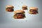 Freshly made three burgers fall on gray background. Creative concept of floating fast food. Background of falling burgers.