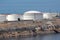 Freshly painted new large industrial white metal oil refinery tanks on top of rocky sea shore connected with metal pipes to pier