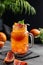 Freshly squeezed blood orange juice with ice, mint and a slice of fruit in a jar on a dark background with citrus fruits and palm