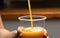 Freshly squeezed orange juice stream pouring into take-out plastic disposable glass held in a hand of a young man, close-up shoot