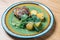 Fried baked duck served on a green plate with slices of potatoes and herbs