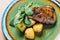 Fried baked duck served on a green plate with slices of potatoes and herbs