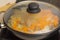 Fried chicken hearts with vegetables, carrots, onion, greens on a black frying pan, closed the glass cover. Background