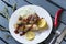 Fried chicken legs with onion, ketchup, lemon ,rosemary on a white plate, rosemary, chili ,fork, knife, grey wooden surface ry,