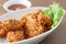 Fried chicken in white bowl served with chili sauce on brown placemat