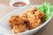 Fried chicken in white bowl served with chili sauce on brown placemat