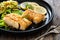 Fried codfish loin served with cabbage salad and lemon slices on black plate on wooden table