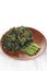 fried cooked green vegetables called kailan are served on a brown wooden plate.  on solid white background