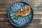 Fried crucian carp with onion and sauce dot painting on a plate on a wooden background. Top view