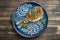Fried crucian carp with onion and sauce dot painting on a plate on a wooden background. Top view