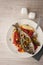 Fried dorado with vegetables, lemon and fork on the ceramic plate top view