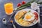 Fried egg with bacon in a white plate with fried pieces of bread, greens, tomatoes, french fries and a glass of fresh juice