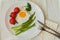 Fried egg with fresh asparagus, tomatoes on the white plate with napkin, fork and knife. Healthy breakfast. Top view