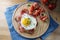 Fried egg and ham on a dark whole meal bread, tomatoes, onion rings and herbs garnish, served on a kitchen board and a blue napkin