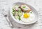 Fried egg, salad with cucumbers, radishes and green peas, toast with feta cheese on a light ceramic plate on wooden background.