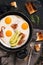 Fried eggs with bacon are served in a frying pan with avocado. A delicious hearty breakfast in a rustic style on a dark background