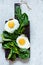 Fried eggs for breakfast with fresh spinach on rye bread toast. Hearty tasty breakfast on a blackboard