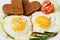 Fried eggs with fresh vegetables and toast in shape of heart on white plate