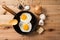 Fried eggs, in a frying pan, on wooden background. Top wiew