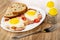 Fried eggs with gammon and tomato, pieces of bread in dish, salt and pepper shakers, fork on wooden table