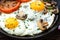 Fried eggs with mushrooms and tomato on dark wooden table