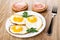 Fried eggs with parsley in plate, sandwiches with sausages, fork on table