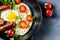 Fried eggs with sausages, tomatoes and microgreens on a black plate. Generative AI