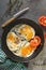 Fried eggs with tomato and thyme and spices on a black skillet on a gray background, knife, towel in a green cage