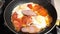 Fried eggs with tomatoes and bacon fried in a frying pan close-up