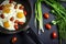 Fried eggs with tomatoes in a pan and fresh onions on dark background . Top view