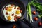 Fried eggs with tomatoes in a pan and fresh onions on dark background . Top view