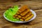 Fried fish fingers on a plate with lettuce on wooden table