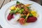 Fried fish on vegetables like carrots, cauliflower, beet and tomatoes with saffron sauce and foam, garnished with herbs and