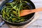 Fried garlic arrows in a frying pan and on a vintage wooden table. Simple and healthy vegetable food