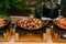 Fried halves of potatoes, in a skillet on the stove, with fried sausages and chopped tomato rings on a buffet table at