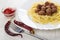Fried meatballs with spaghetti in dish, bowl with ketchup, chili peppers, fork on wooden table