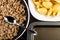 Fried mincemeat, spoon in frying pan, boiled pasta in plate, dripping pan on wooden table. Top view