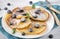 Fried pancakes with fresh blueberries with powdered sugar and mint leaves on a plate, knife and fork on a blue napkin, on a white