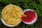 Fried pancakes and red jam on plates among green leaves and grass