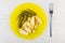 Fried pieces of potato, pickled gherkins in yellow plate, fork