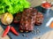 Fried pork ribs and with baked potatoes, chili peppers and lettuce leaves on a black stone tray, close-up.