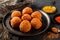 Fried potato cheese balls or croquettes with spices on black plate over dark stone background. Unhealthy food